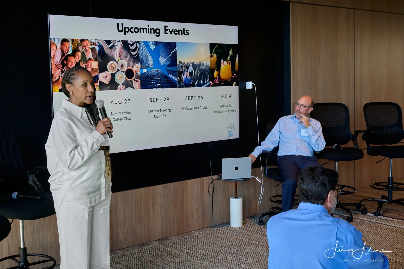 A chapter leader with a microphone presenting a slide of upcoming events to members