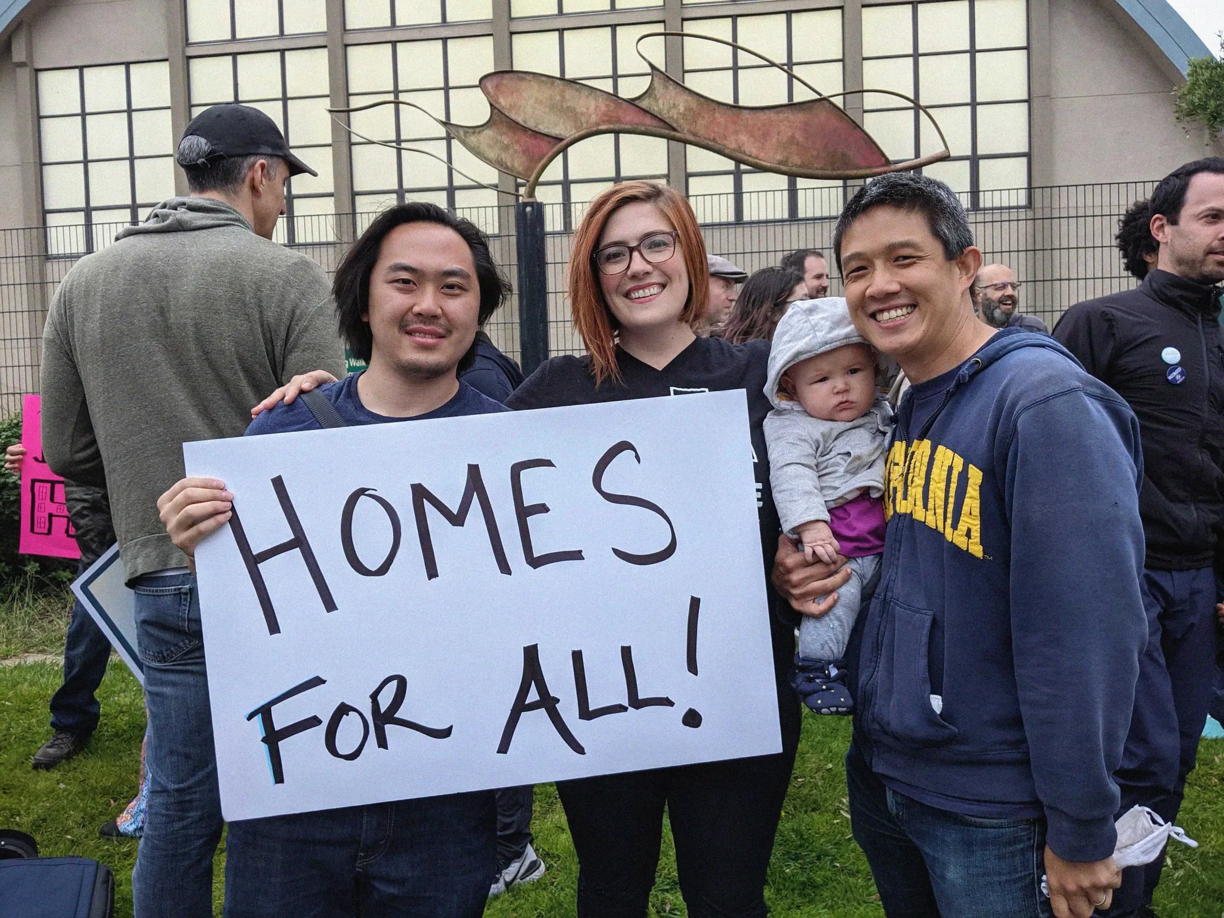 Members holding a hand-painted “Homes for all!” sign at a rally