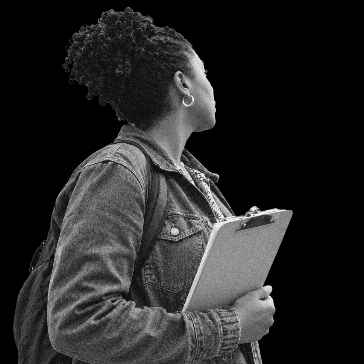 An organizer in a denim jacket holding a clipboard, looking up over a city street map