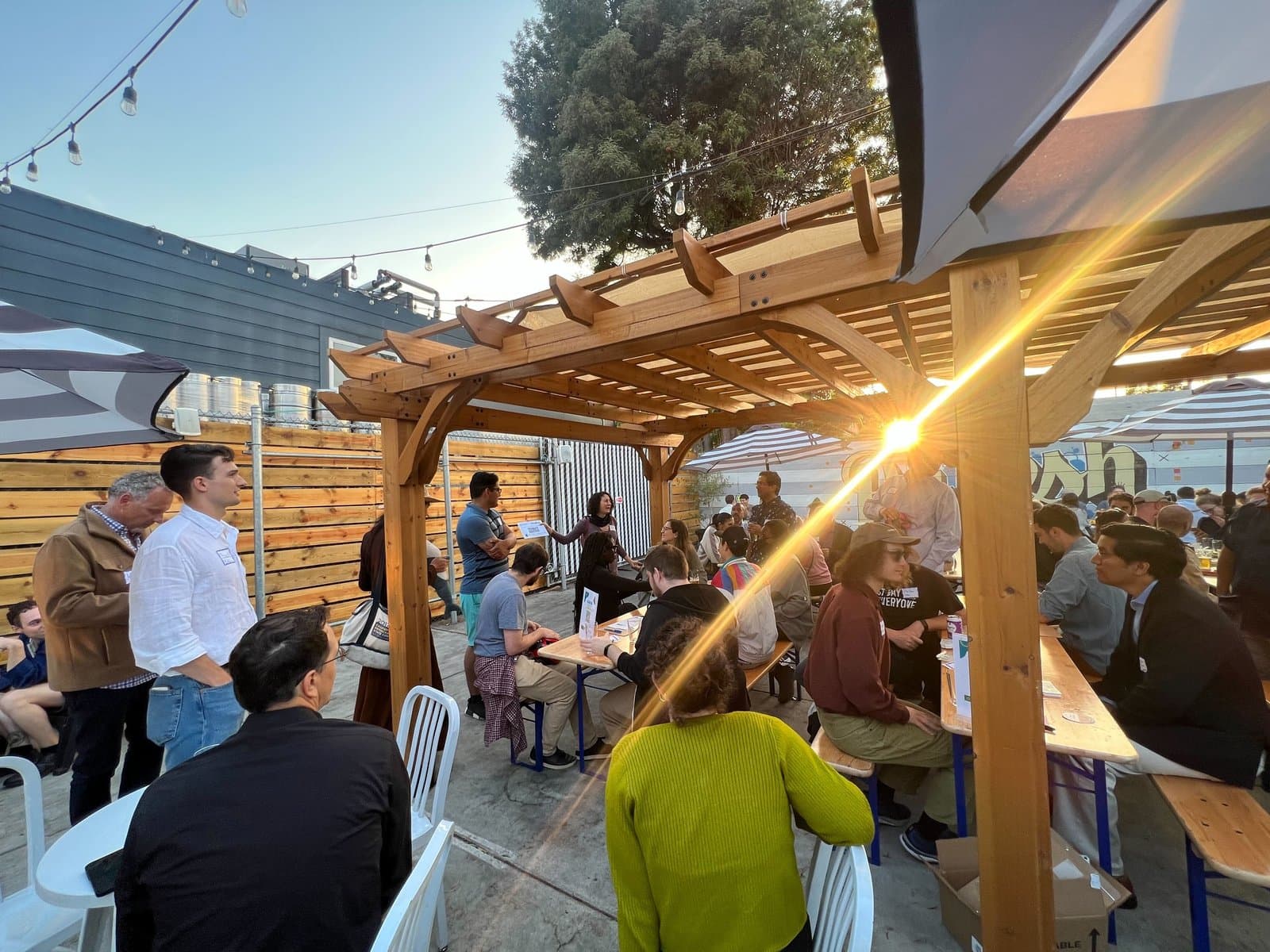 Members mingling at an outdoor chapter happy hour under a pergola at sunset