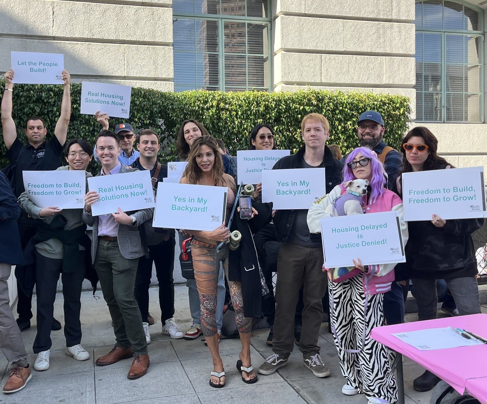 YIMBY Los Angeles members outside City Hall with signs reading Yes in my backyard and Let the people build